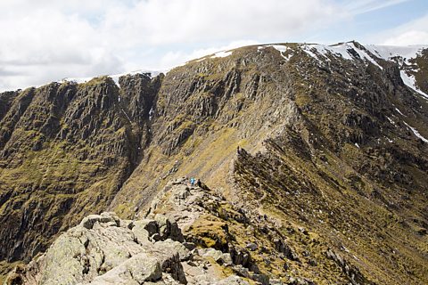 A photo of the top of a mountain which goes up to form a sharp peak with sides that drop sharply either side.