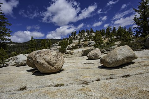 Large rocks seemingly out of place on a flat rock surface surrounded by trees.