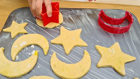 Eid biscuit bakes on a tray with cookie cutters. The shapes are moons and stars.