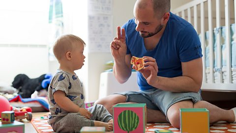 Father playing with son and using hand gestures to communicate. They sit on the floor of the son's room.