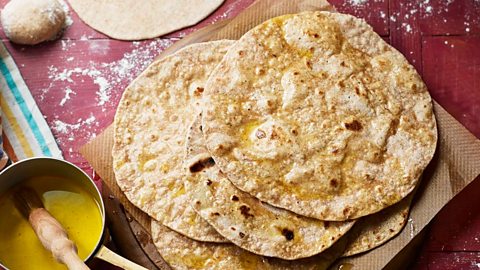 Rotis on a board next to a pan of ghee