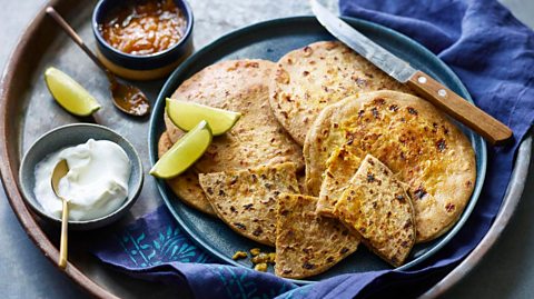 A tray of keema paratha with lemons, yoghurt and chutney