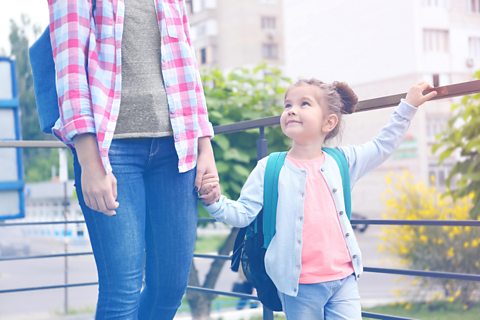 Girl and parent walk down the street together.