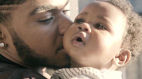 A close up of a dad and his 6-month-old son. Dad is kissing his son's cheek.