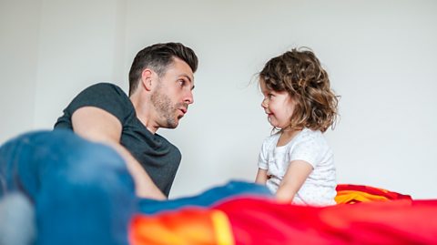 father and daughter laid on bed chatting 