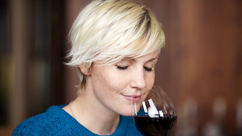 A woman smells red wine in a glass