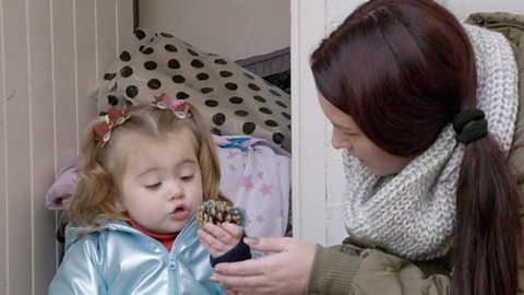 A mum and her daughter are looking at a pine cone in Tiny Happy People's treasure box activity.