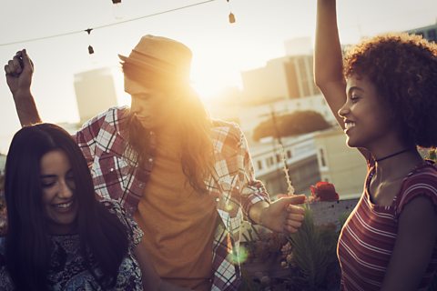 a picture of two young women and a young man dancing on a rooftop with sunshine in the background