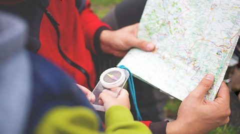 Two people hold a map and compass.