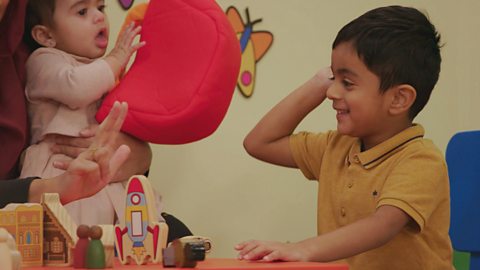 A boy and his little sister play with a wooden rocket ship at the Toddler Club.