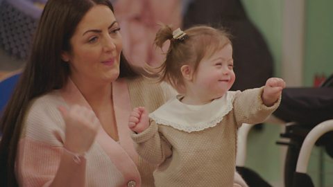 A toddler and her mum sit in the toddler club and listen to a story with Gemma and Nigel.