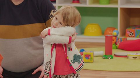 A young girl in the toddler club pretend to hug a tree as part of the nature story with Nigel Clarke.