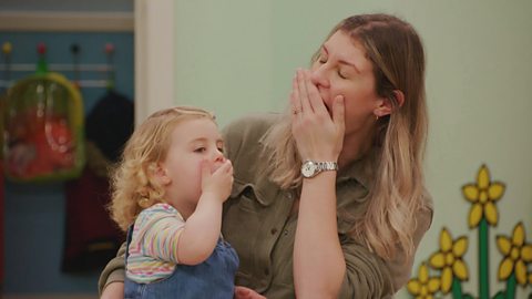 A mum and her child are yawning together at the Toddler Club. Their hands are over their mouths.