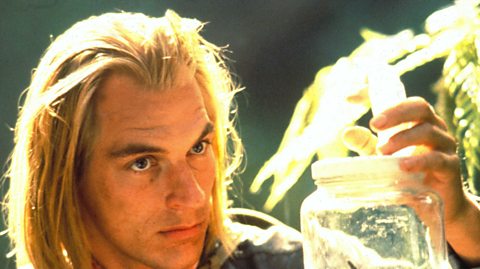 A photo of actor Julian Sands holding a jar with a spider in it.