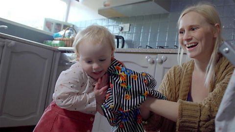 A mum and her daughter are hanging up the laundry in the kitchen. The little girl is hugging an item of clothing.