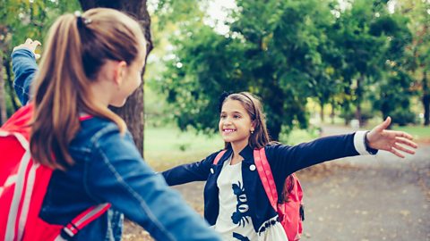 Two girls meet in the park, about to hug each other.