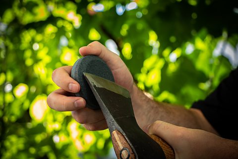 A person sharpening the edge of an axe using a grindstone.