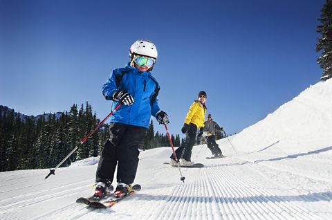 A person skiing down a hill on snow, behind them is another person on a snowboard