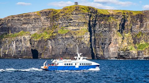 A photograph of a boat sailing past a cliff