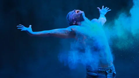 Henrik Sorensen/Getty Images Man stretching out arms is covered in blue powder (Credit: Henrik Sorensen/Getty Images)