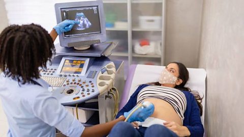 A nurse performing an ultrasound scan  on a pregnant lady wearing a face mask  