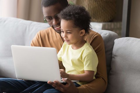 Little boy and dad play on laptop together.