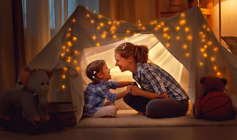 Little girl and parent laugh together under fairy lights.