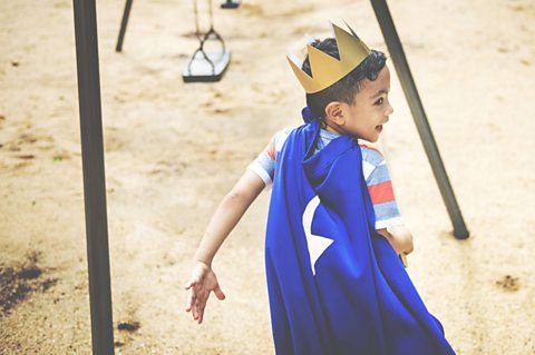 Little boy in a crown and robe running outside.