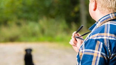 A dog blurred in the background with close up of dog owner using training whistle