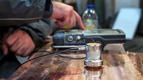 a person pushing buttons on an ultrasound scan which is positioned onto metal to look for faults within pipe