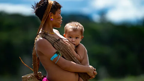 Getty Images A Yanomami mother breastfeeds her baby as she waits at a health care centre in Brazil (Credit: Andressa Anholete / Getty Images)