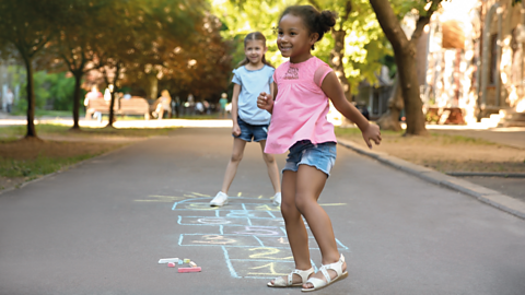 Two girls play hopscotch together.