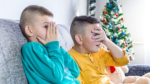 Two kids watch tv with eyes over their eyes, scared