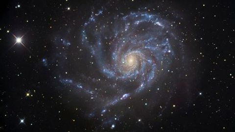 Pin wheel galaxy circular blue and white lights surrounded by small white stars on a black back drop with a yellowed misted centre