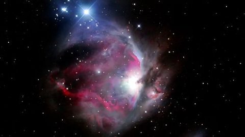 Orion Nebula in outer space on black back drop small white dotted stars centred dark pink white and soft blue colours in a cloud like circle formation 