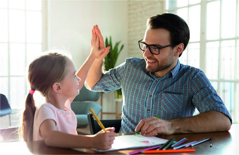 Little girl does homework at a table with parent.