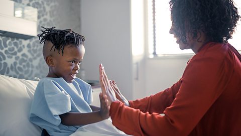 A little boy in a hospital bed high fiving his mum.