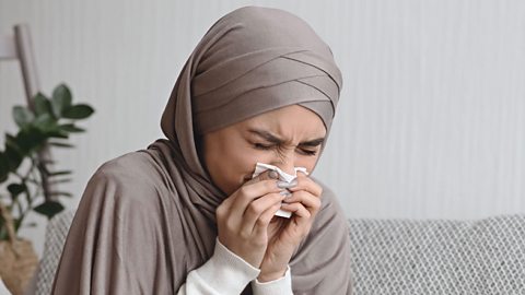 A woman sneezes into a tissue