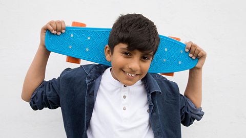 A boy holds a skateboard behind his head