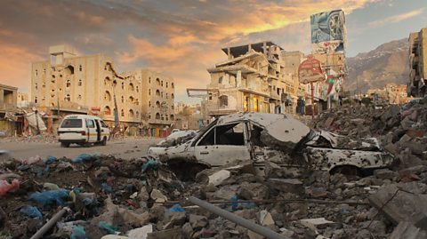 Debris, car damage in a war zone of Taiz city in Yemen, buildings falling down barely standing flattened damaged cars surrounded by rubble.