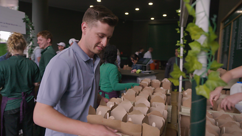 A photograph of a young man called Joe, wearing a light blue polo shirt, carrying boxes of strawberries at Wimbledon.