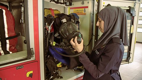 A lady wearing a hijab headscarf, inspecting some breathing equipment on a red fire truck.