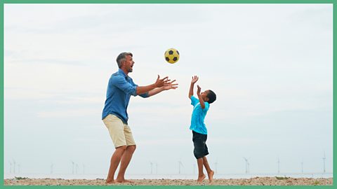 A dad and son playing catch with wind turbines far behind them