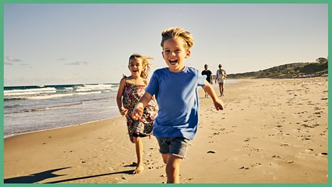 Kids running on a beach, with their parents behind them