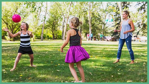 A mum and 2 daughters passing a ball between each other in the air