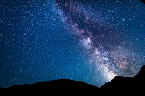 Light strip in the night sky vertical to the centre of the frame light blue dark blue and white colours surrounding and within strip over a lake at night