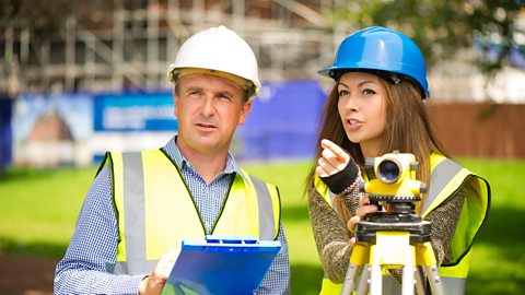 An image of two construction workers on site, wearing high-vis jackets and hard hats