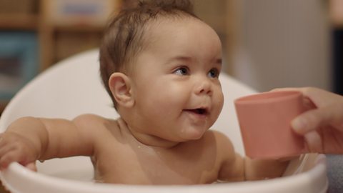 A baby girl in the bath smiling at her dad.