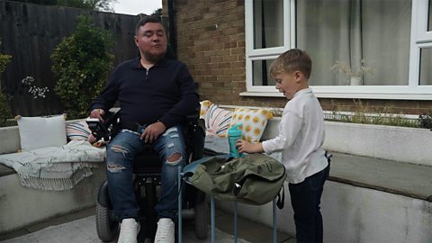 4-year-old Rowan and his dad, who sits in a wheelchair, are packing a bag together in their garden.