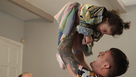 A dad lifting his little girl up over his head.